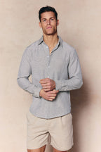 Man in an ecru/navy striped Abilo shirt with an open collar, chest pocket, and tailored fit, paired with beige shorts.