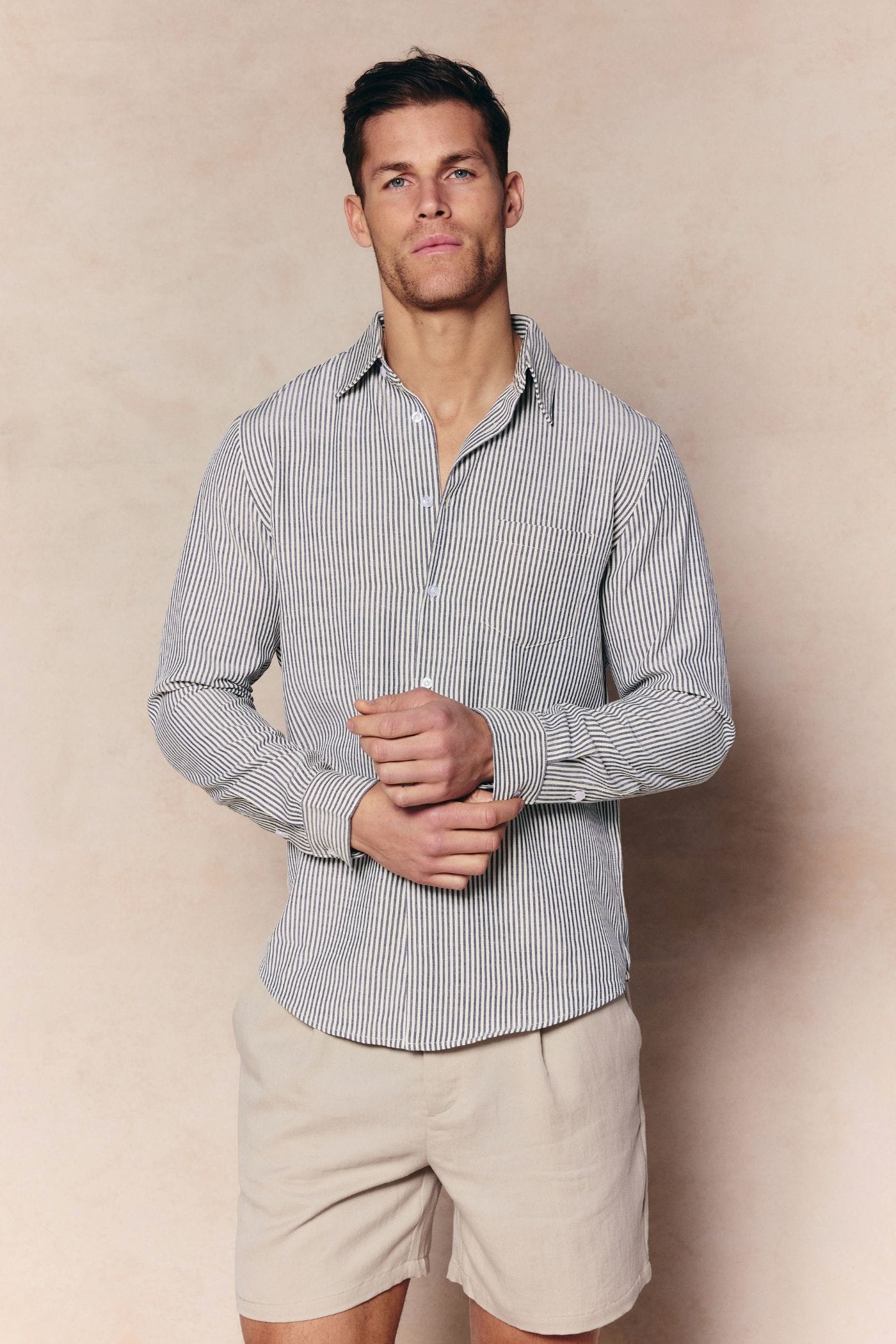 Man in an ecru/navy striped Abilo shirt with an open collar, chest pocket, and tailored fit, paired with beige shorts.