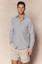 Man wearing an Abilo Ecru/Navy striped shirt with an open collar and beige shorts.