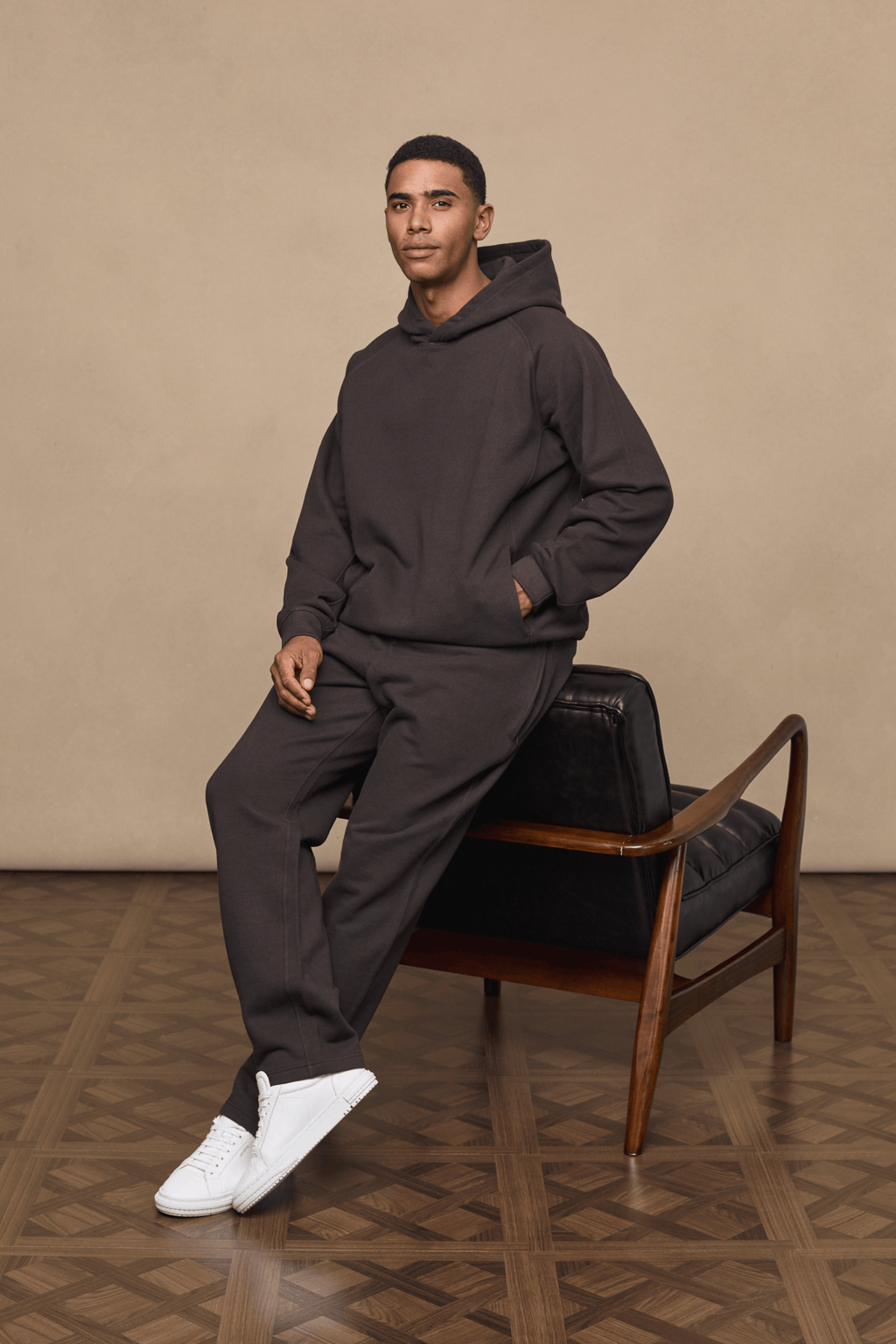 Man in dark brown Axel straight leg jogger and matching hoodie, sitting on a chair.