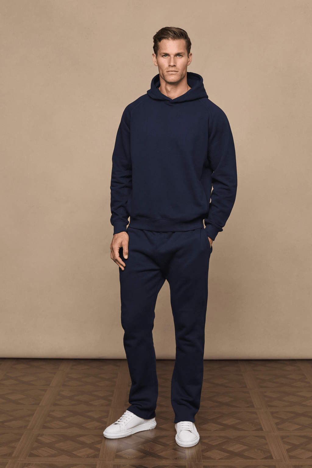 Man wearing a dark navy Axel Straight Leg Jogger and matching hoodie with white sneakers.