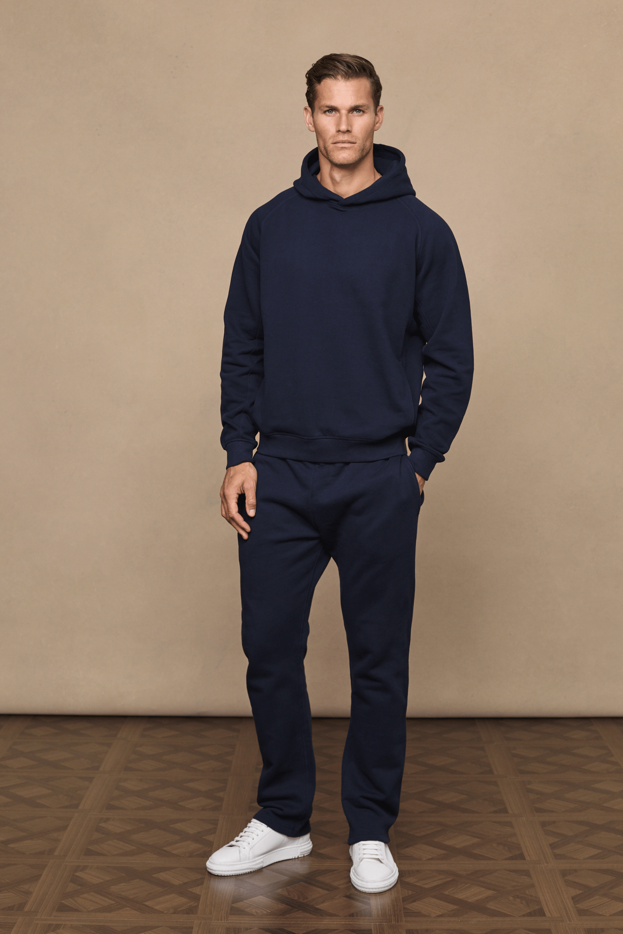 Man wearing a dark navy Axel Straight Leg Jogger and matching hoodie with white sneakers.