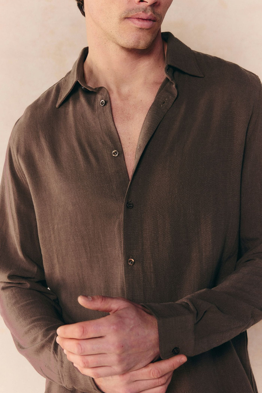 Man wearing a relaxed fit brown linen shirt with a classic collar and open buttons.