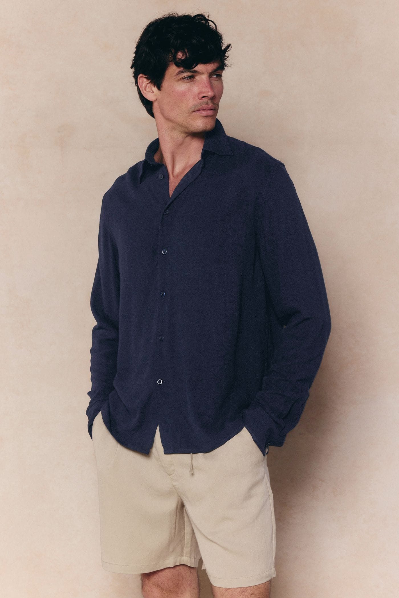 Man in navy Cami Linen Classic Collar Shirt with long sleeves, paired with light beige shorts.