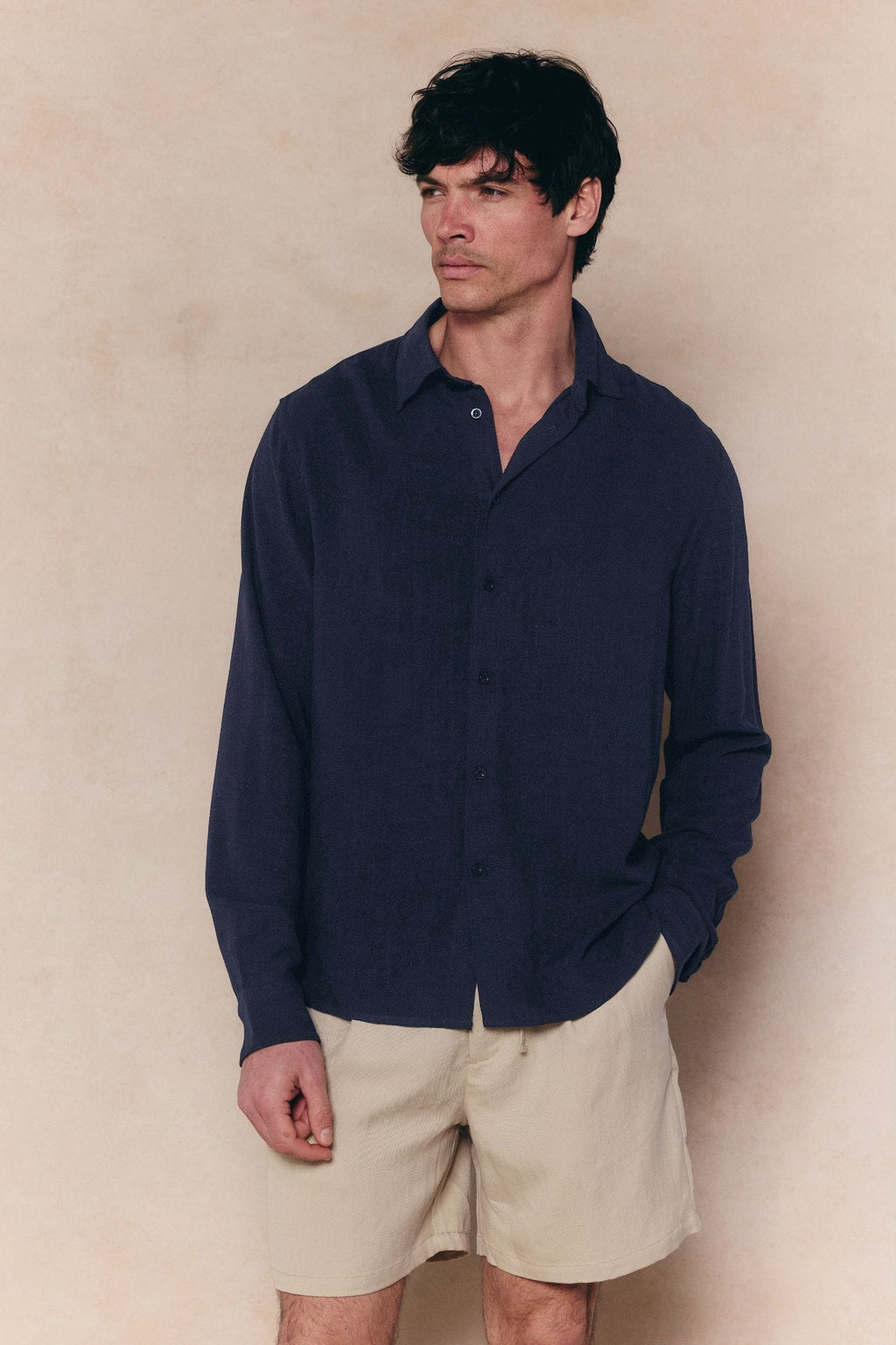 Man wearing a navy Cami Linen Classic Collar Shirt with a relaxed fit and natural texture, paired with beige shorts.