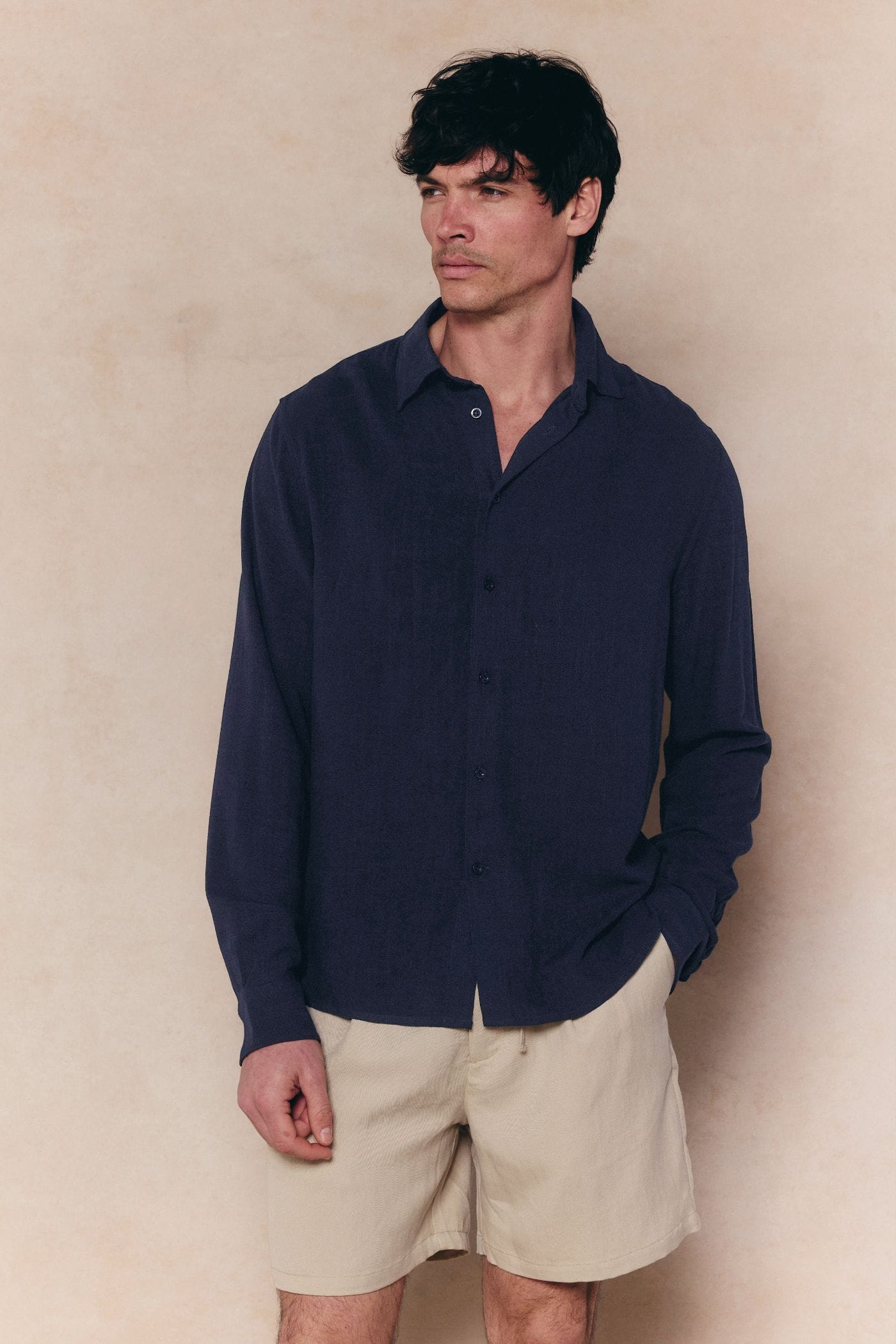 Man wearing a navy Cami Linen Classic Collar Shirt with a relaxed fit and natural texture, paired with beige shorts.