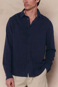 Man wearing a navy Cami Linen Classic Collar Shirt with long sleeves and a relaxed fit, paired with light pants.