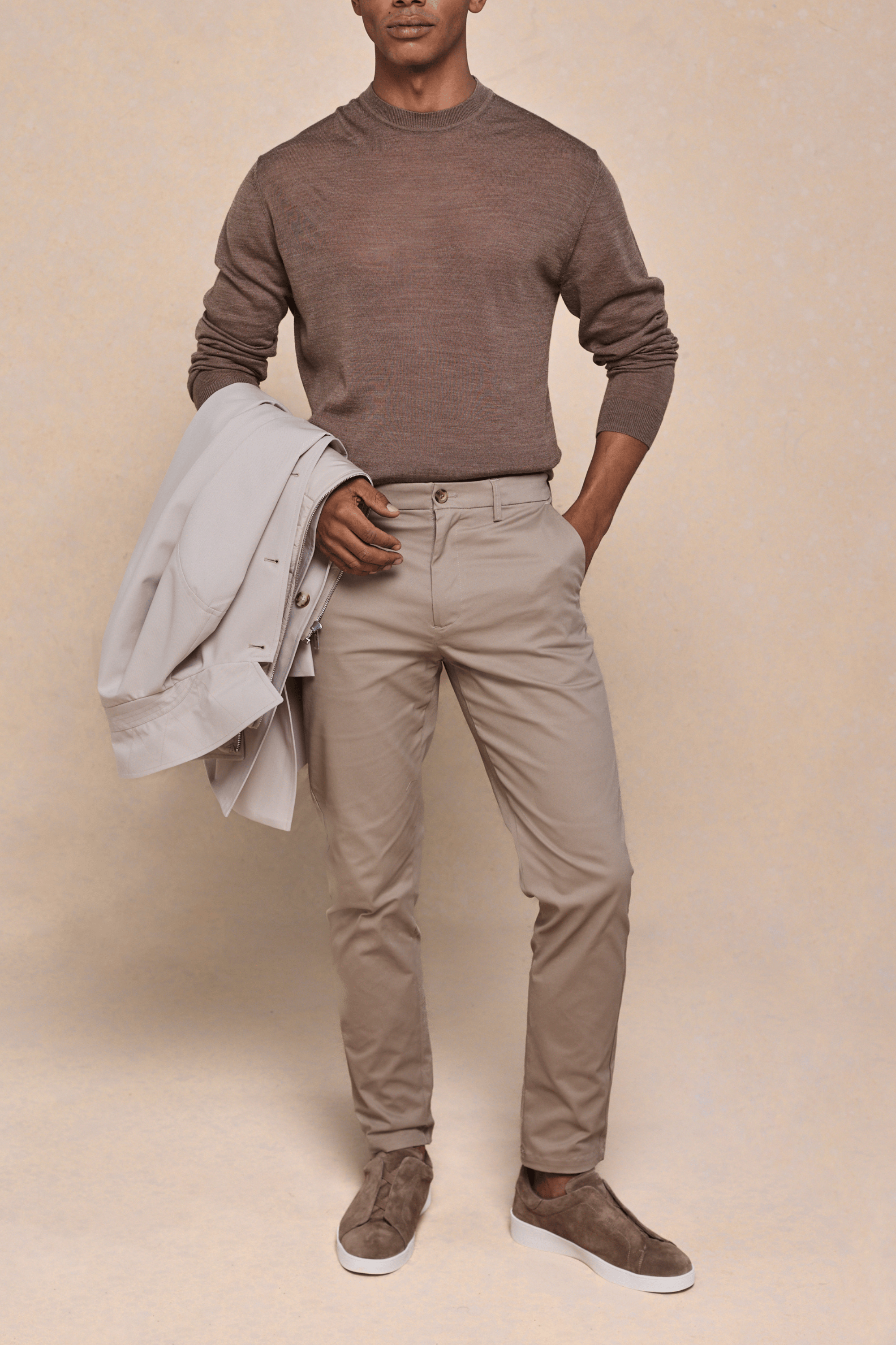 Man wearing beige Elliot Easy Chinos, a brown sweater, and holding a light jacket.