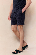 Man wearing navy Fausto flocked towelled shorts and matching shirt, with black slides.