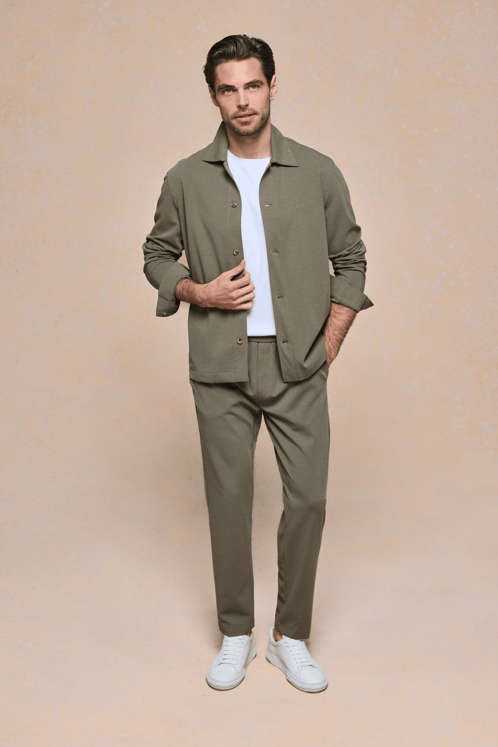 Man in khaki textured overshirt, white tee, matching trousers, and white sneakers.