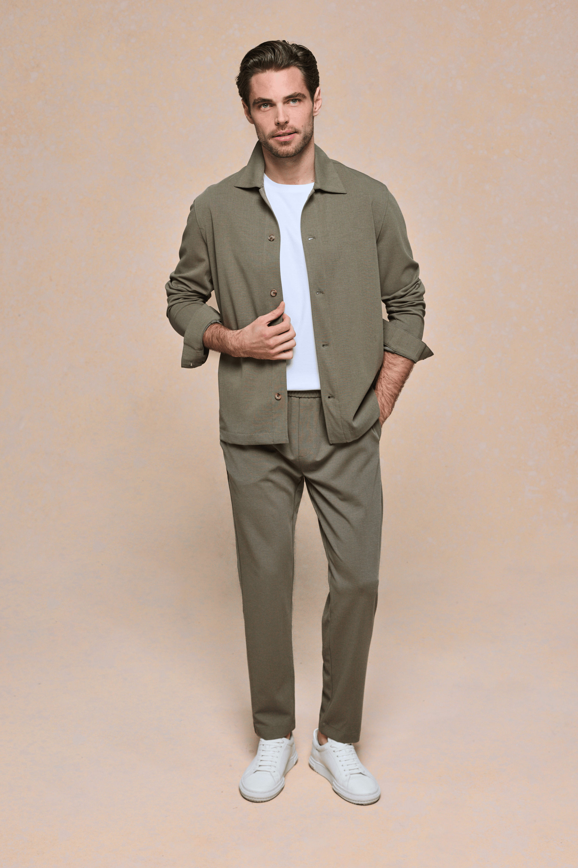 Man in khaki textured overshirt, white tee, matching trousers, and white sneakers.