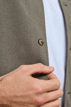 Close-up of a hand adjusting a khaki Geneva Textured Overshirt with a faux horn button.
