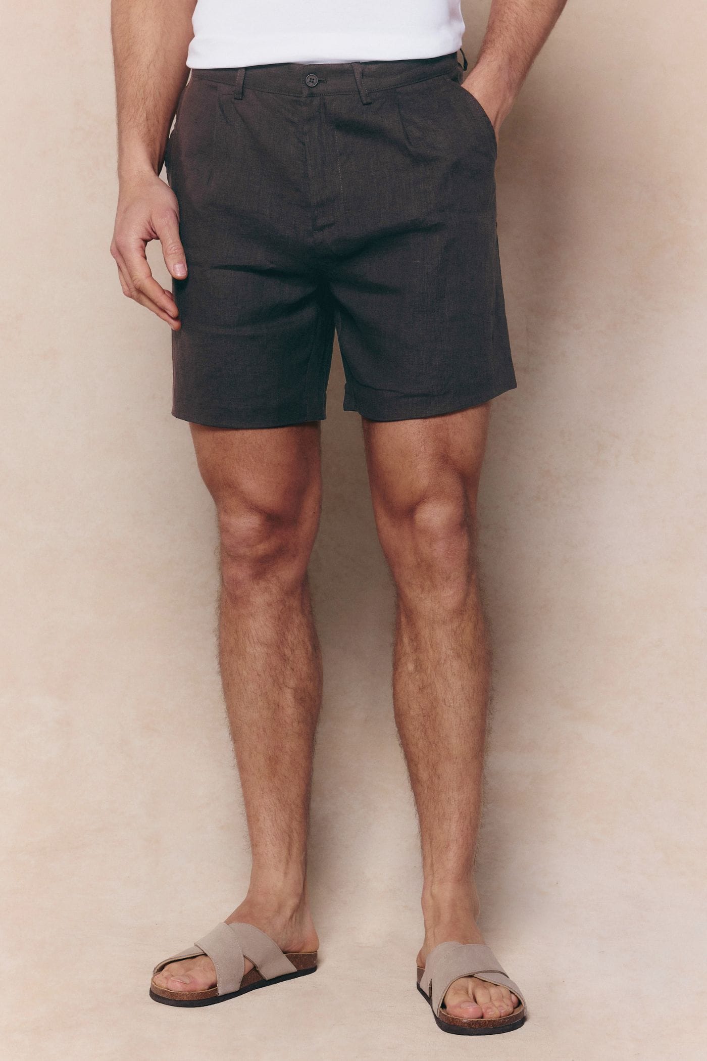 Men's brown pleated waistband linen shorts with side pockets, worn with sandals.