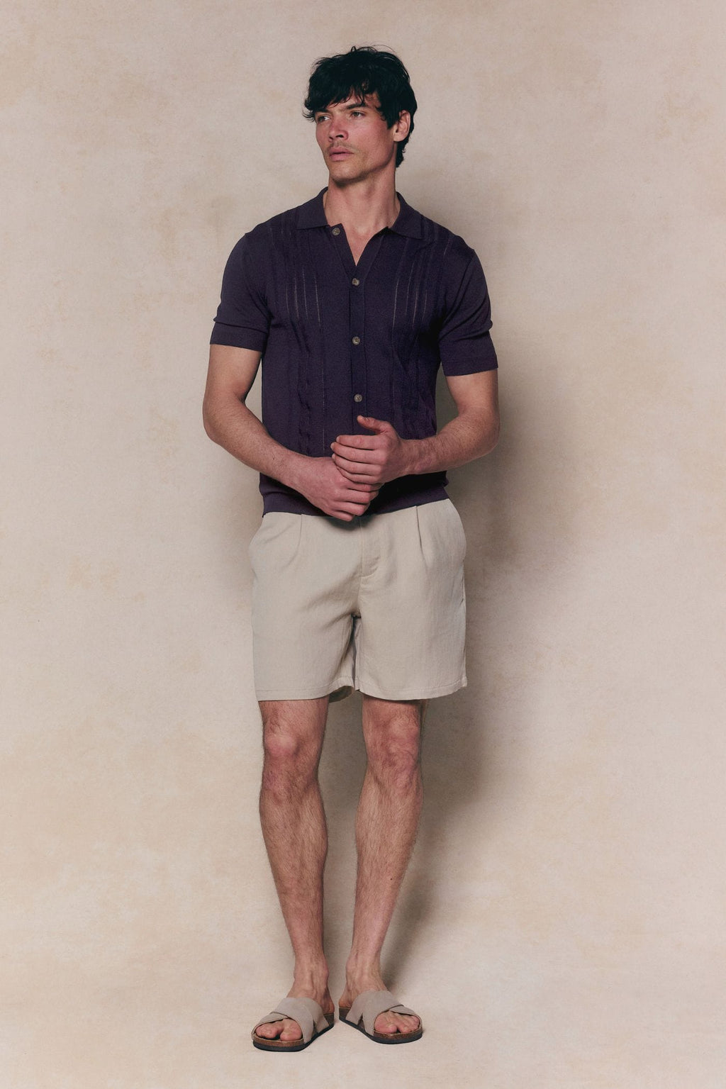 Man in navy boucle knit striped polo, full button-through, with beige shorts and sandals.