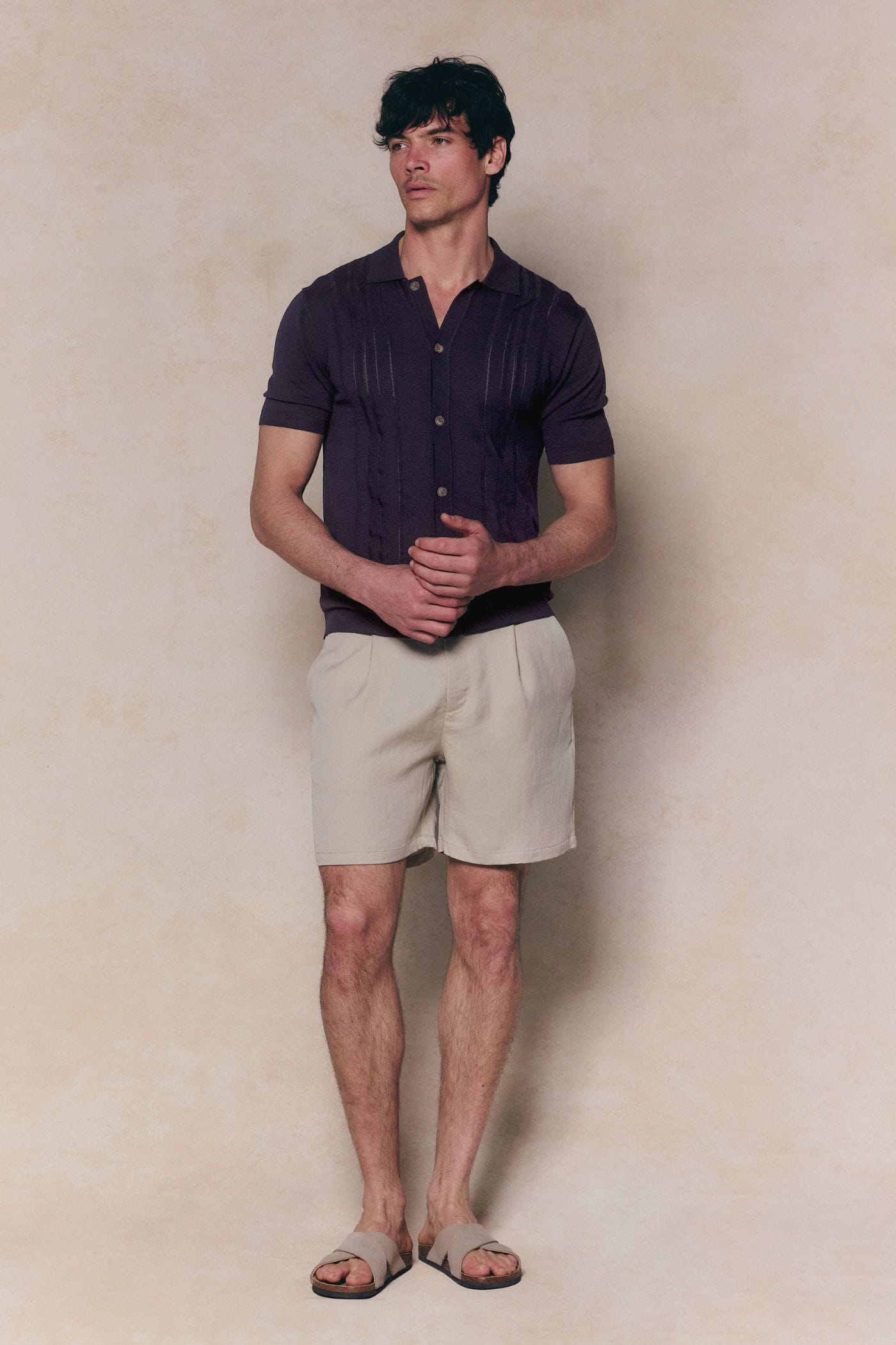 Man in navy boucle knit striped polo, full button-through, with beige shorts and sandals.