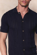 Man wearing a navy boucle knit striped polo with a full button-through front and short sleeves.