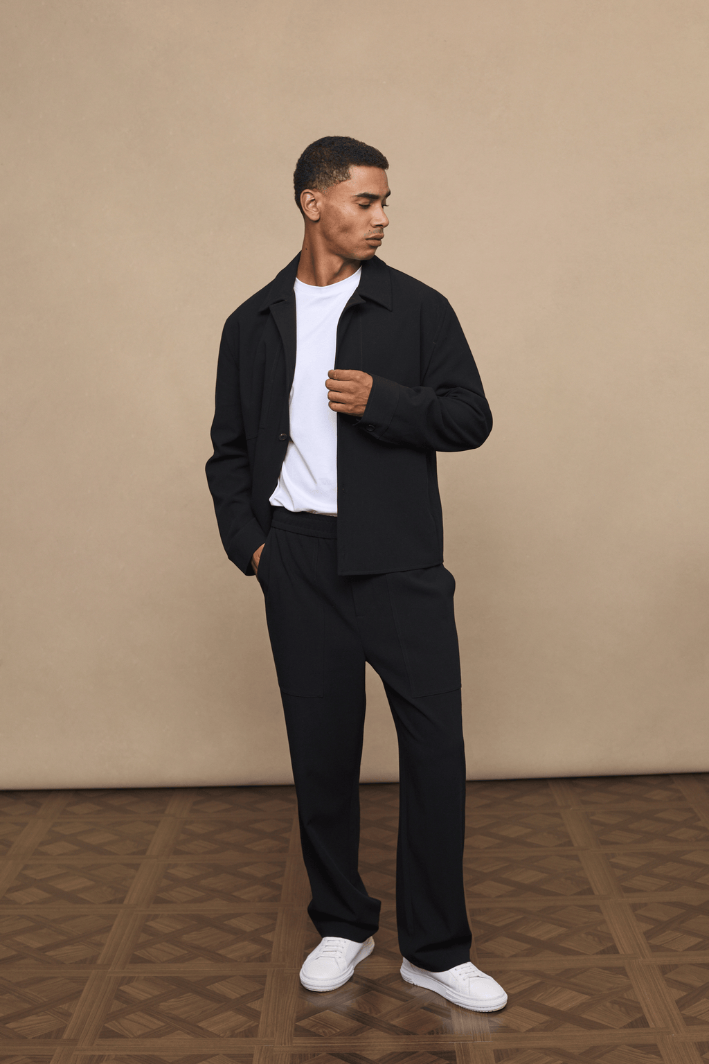 Man in black Julien Relaxed Panelled Trousers and matching jacket with a white t-shirt.