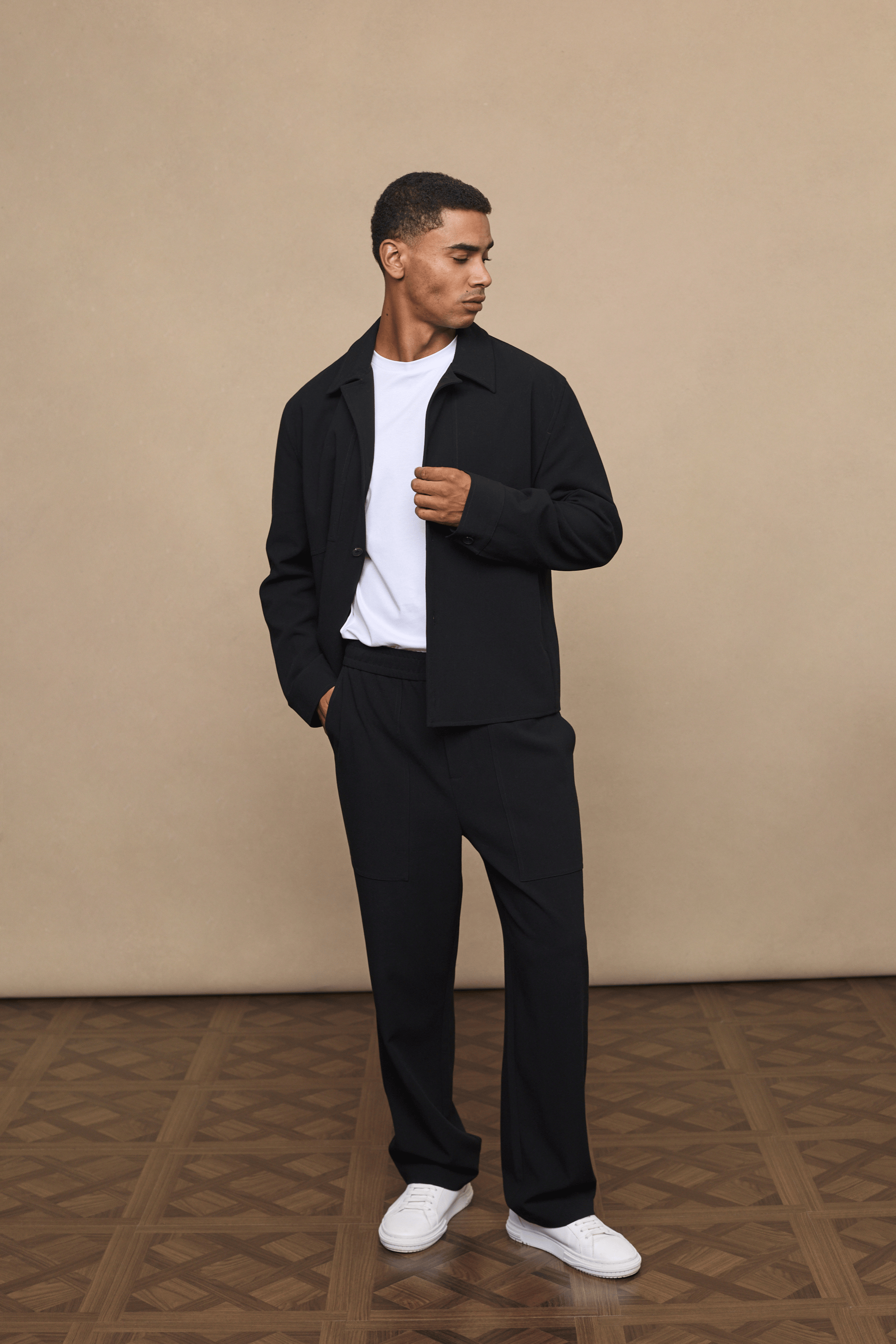 Man in black Julien Relaxed Panelled Trousers and matching jacket with a white t-shirt.
