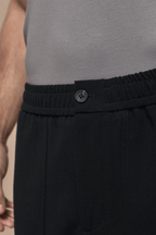Close-up of black Julien relaxed panelled trousers with a branded button fastening and elasticated waist.