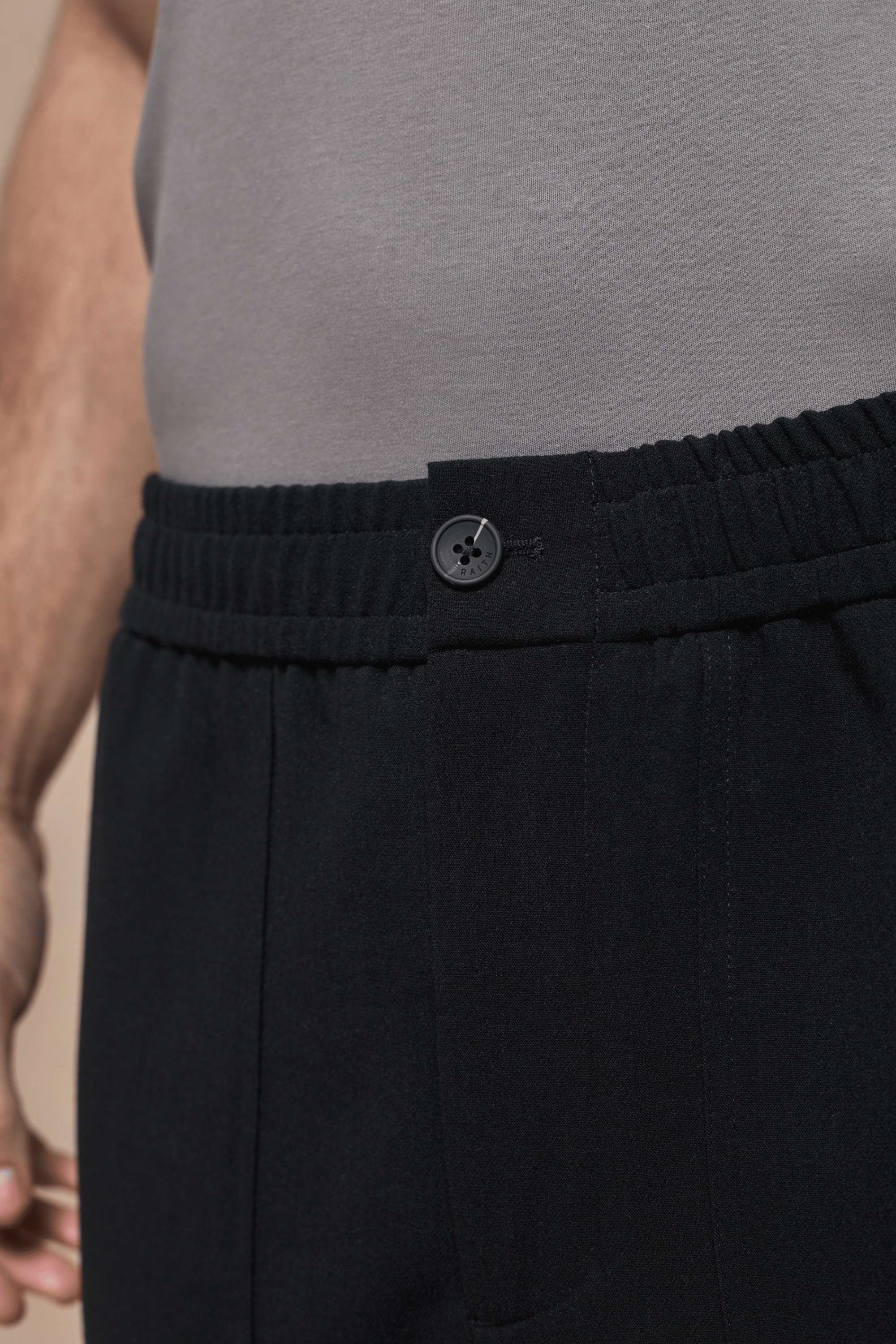 Close-up of black Julien relaxed panelled trousers with a branded button fastening and elasticated waist.