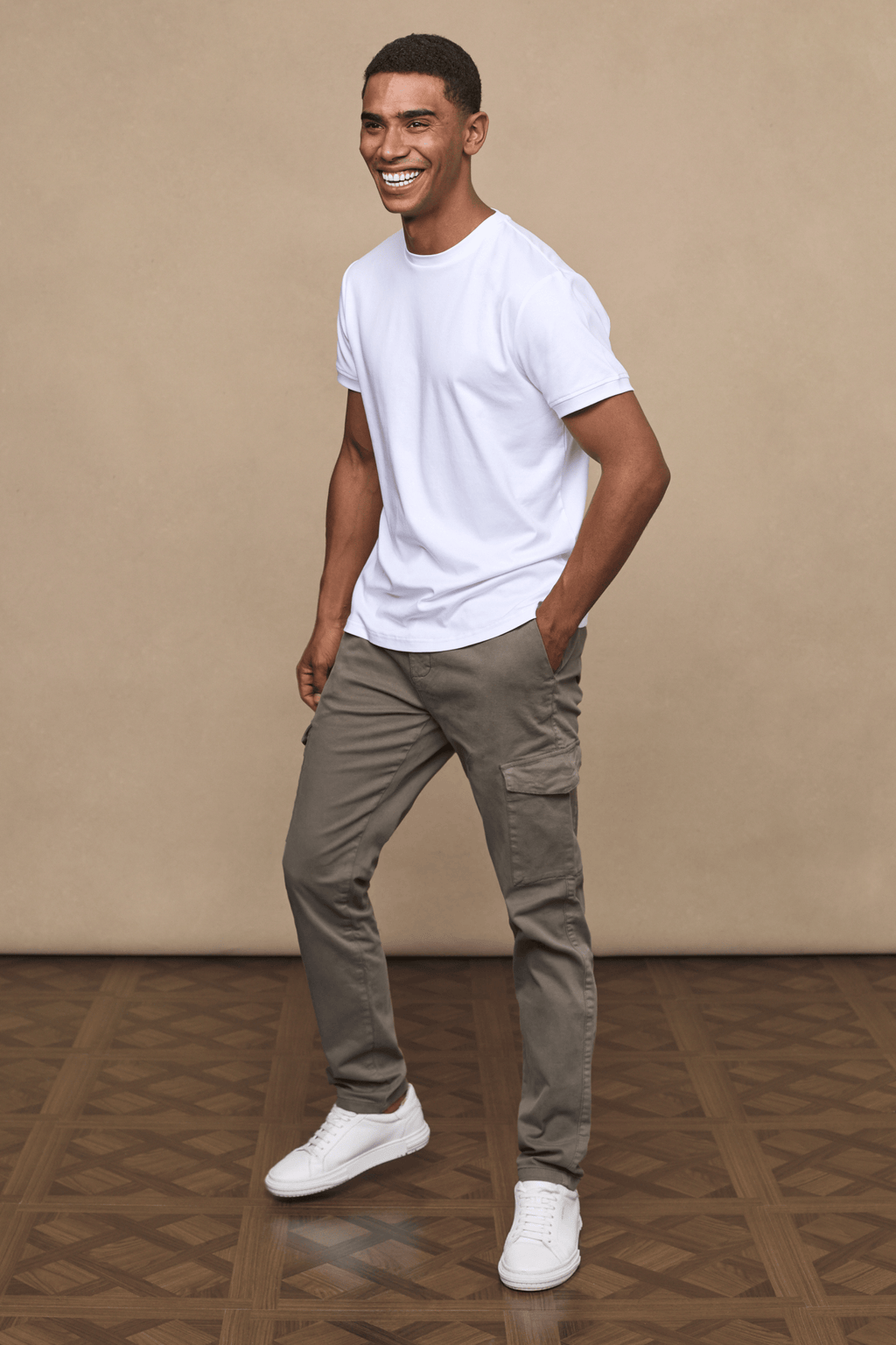 Smiling man in dark olive Lenox Cargo pants with utility pockets, white t-shirt, and white sneakers.