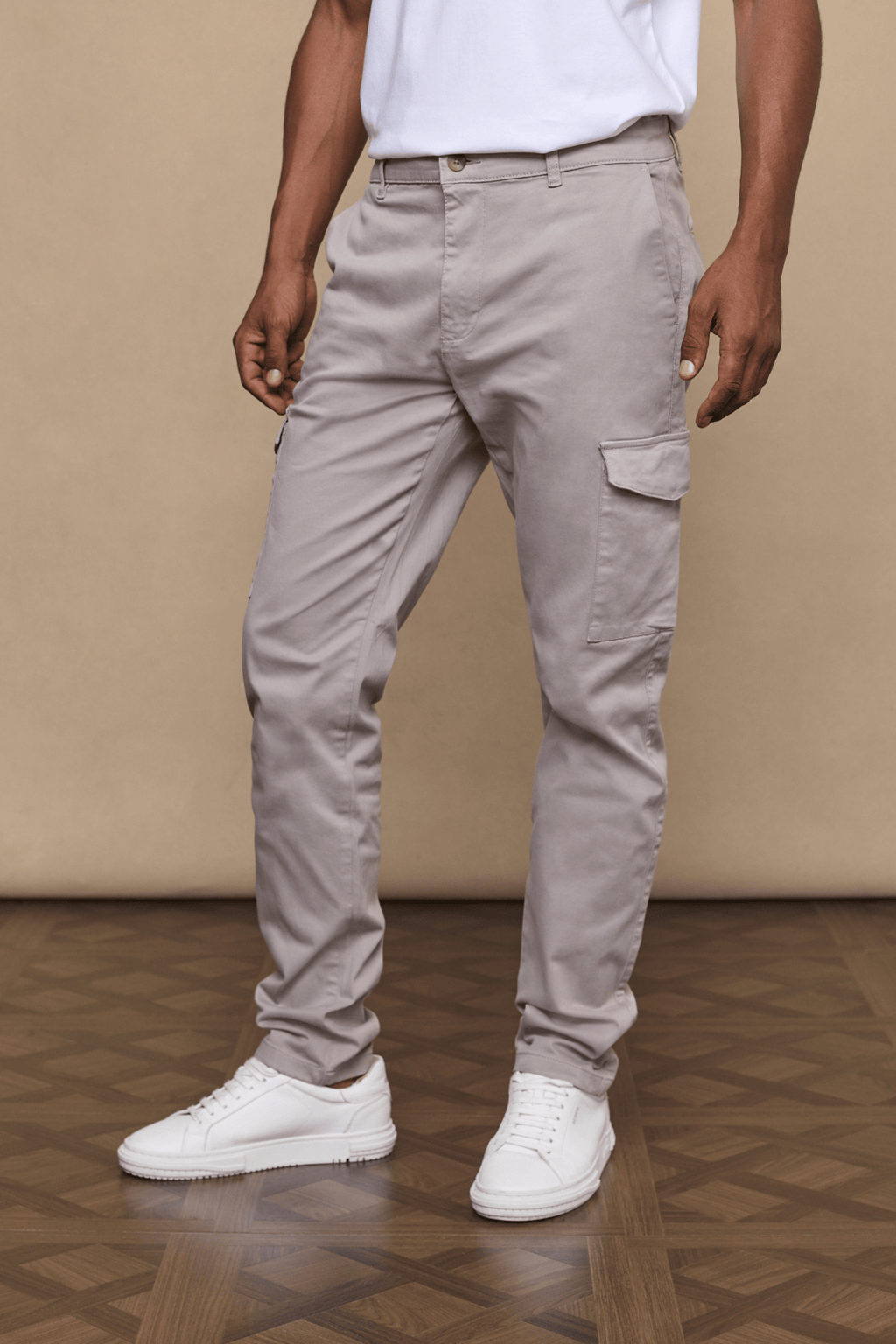 Men's Lenox Cargo Pant in greige cotton-elastane blend, straight leg, utility pockets, worn with white sneakers.