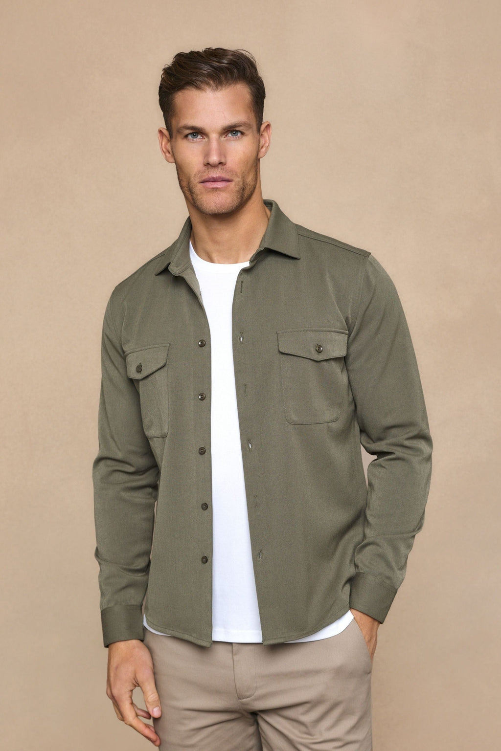 Man wearing a dark olive Leo overshirt with dual chest pockets, over a white t-shirt and beige pants.