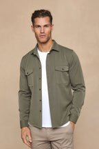 Man wearing a dark olive Leo overshirt with dual chest pockets, over a white t-shirt and beige pants.
