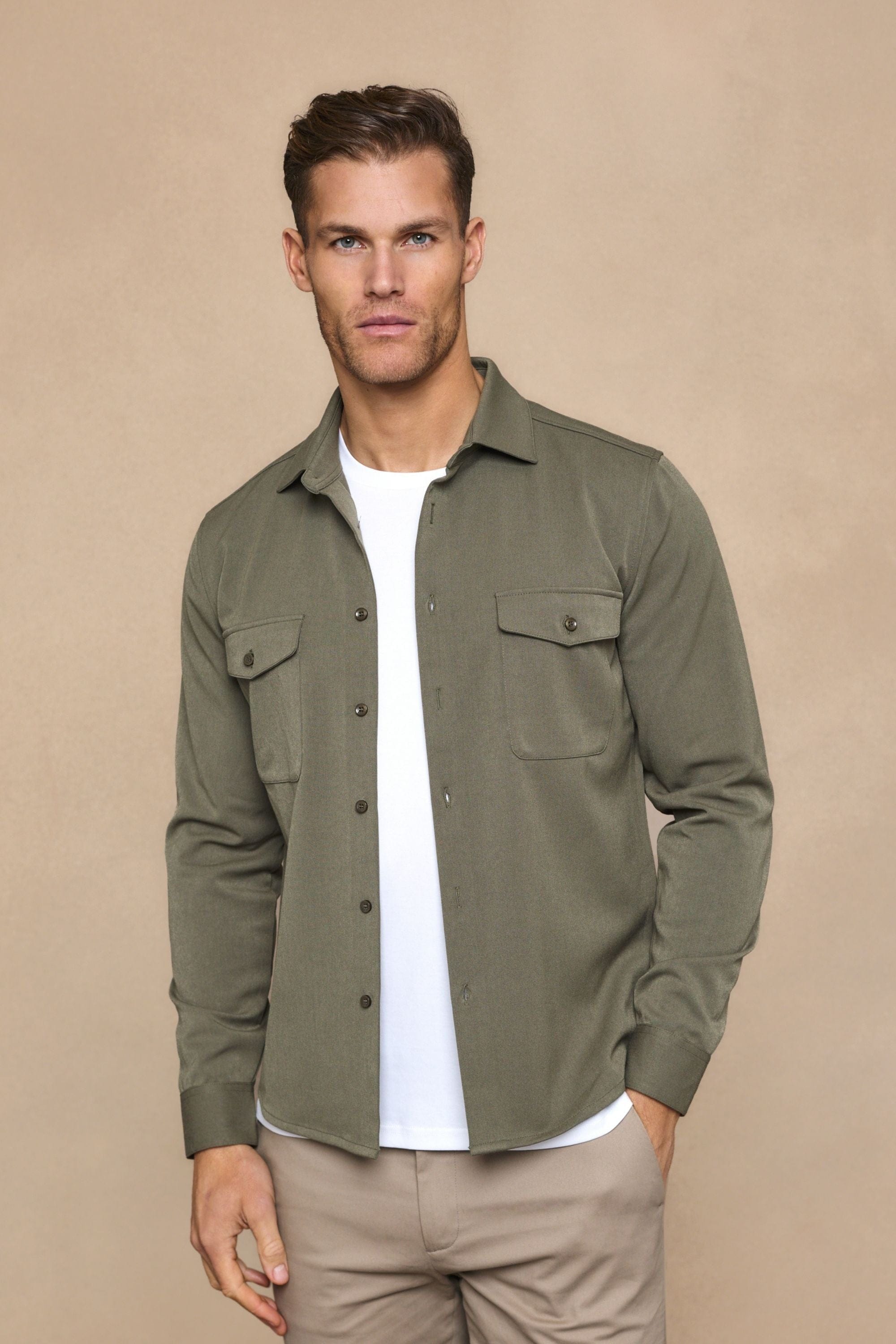 Man wearing a dark olive Leo overshirt with dual chest pockets, over a white t-shirt and beige pants.