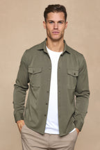 Man wearing a dark olive Leo overshirt with dual chest pockets, open over a white t-shirt and light pants.
