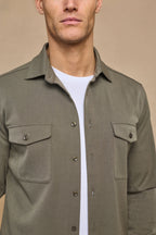 Man wearing a dark olive Leo Overshirt with dual chest pockets and tonal buttons over a white t-shirt.