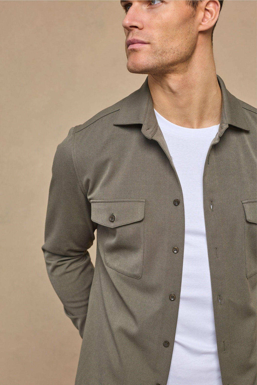 Man wearing a dark olive Leo overshirt with dual chest pockets and tonal buttons over a white t-shirt.