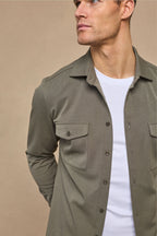 Man wearing a dark olive Leo overshirt with dual chest pockets and tonal buttons over a white t-shirt.