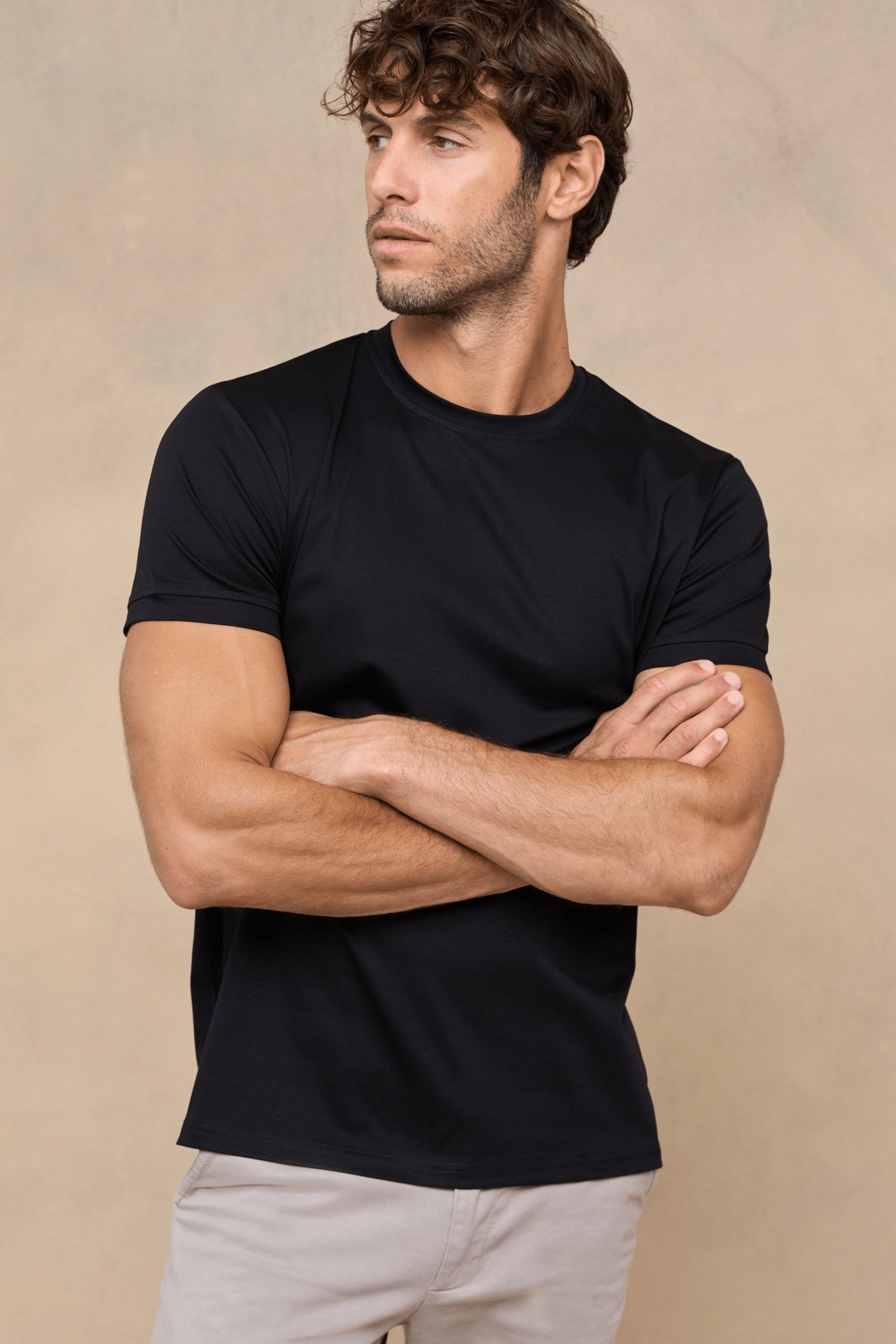 Man wearing a black Luxe Mercerised Cotton Crew-Neck T-Shirt with a subtle sheen, arms crossed.