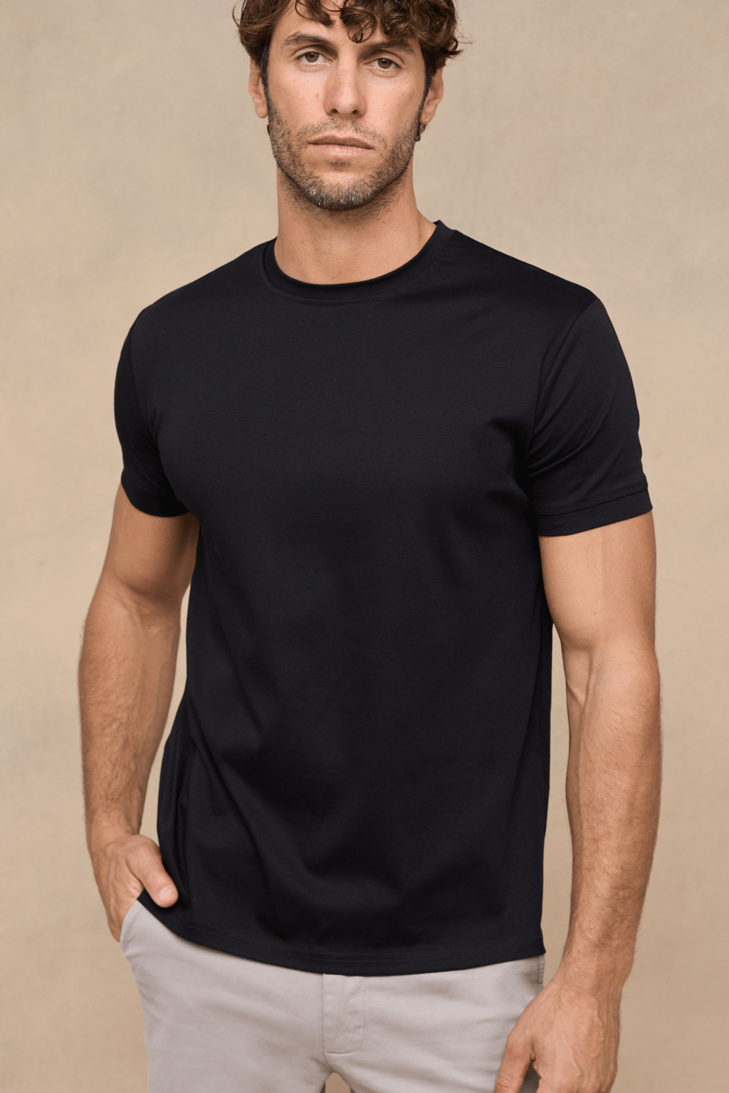 Man wearing a black mercerised cotton crew-neck t-shirt with a subtle sheen, paired with light trousers.