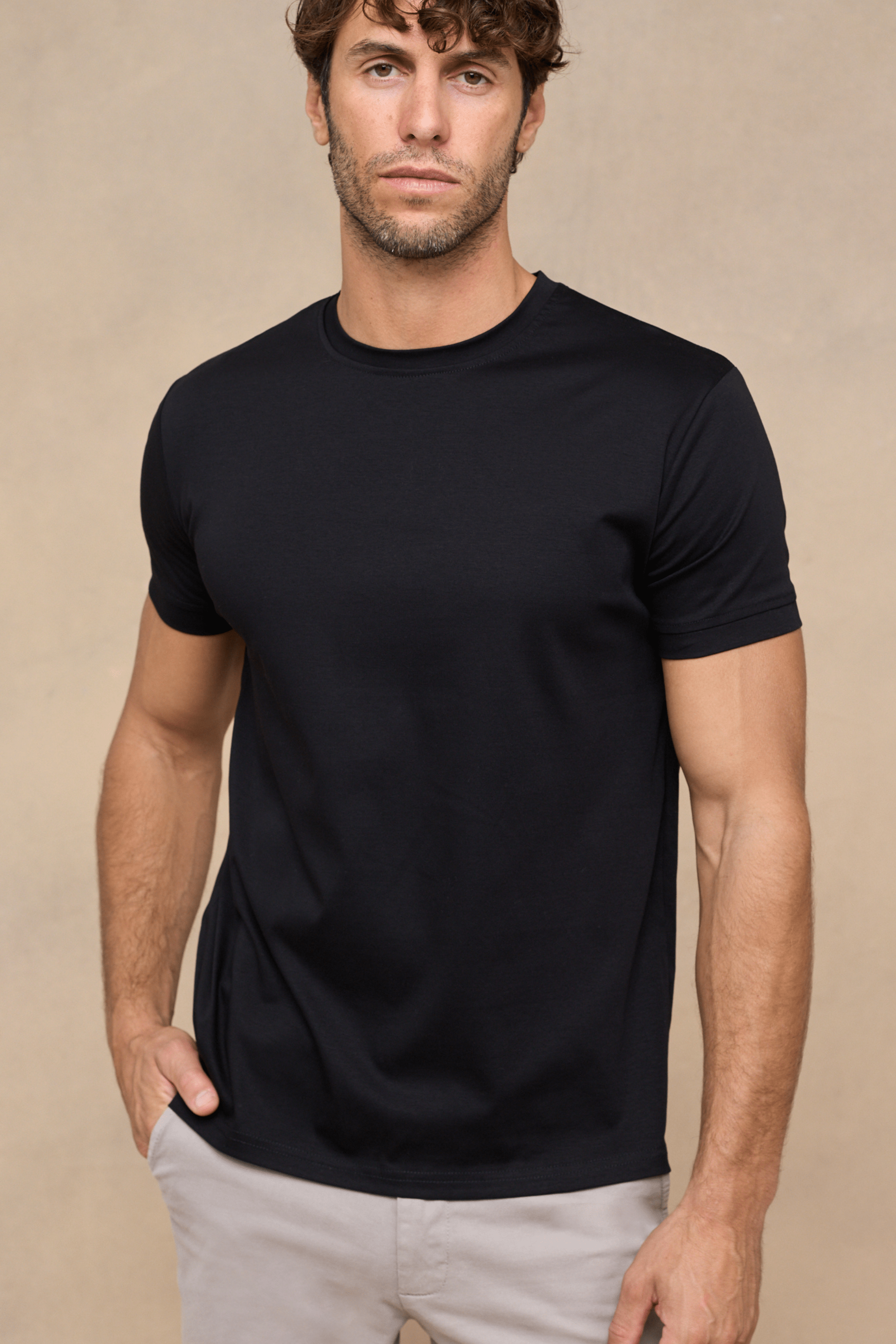 Man wearing a black mercerised cotton crew-neck t-shirt with a subtle sheen, paired with light trousers.