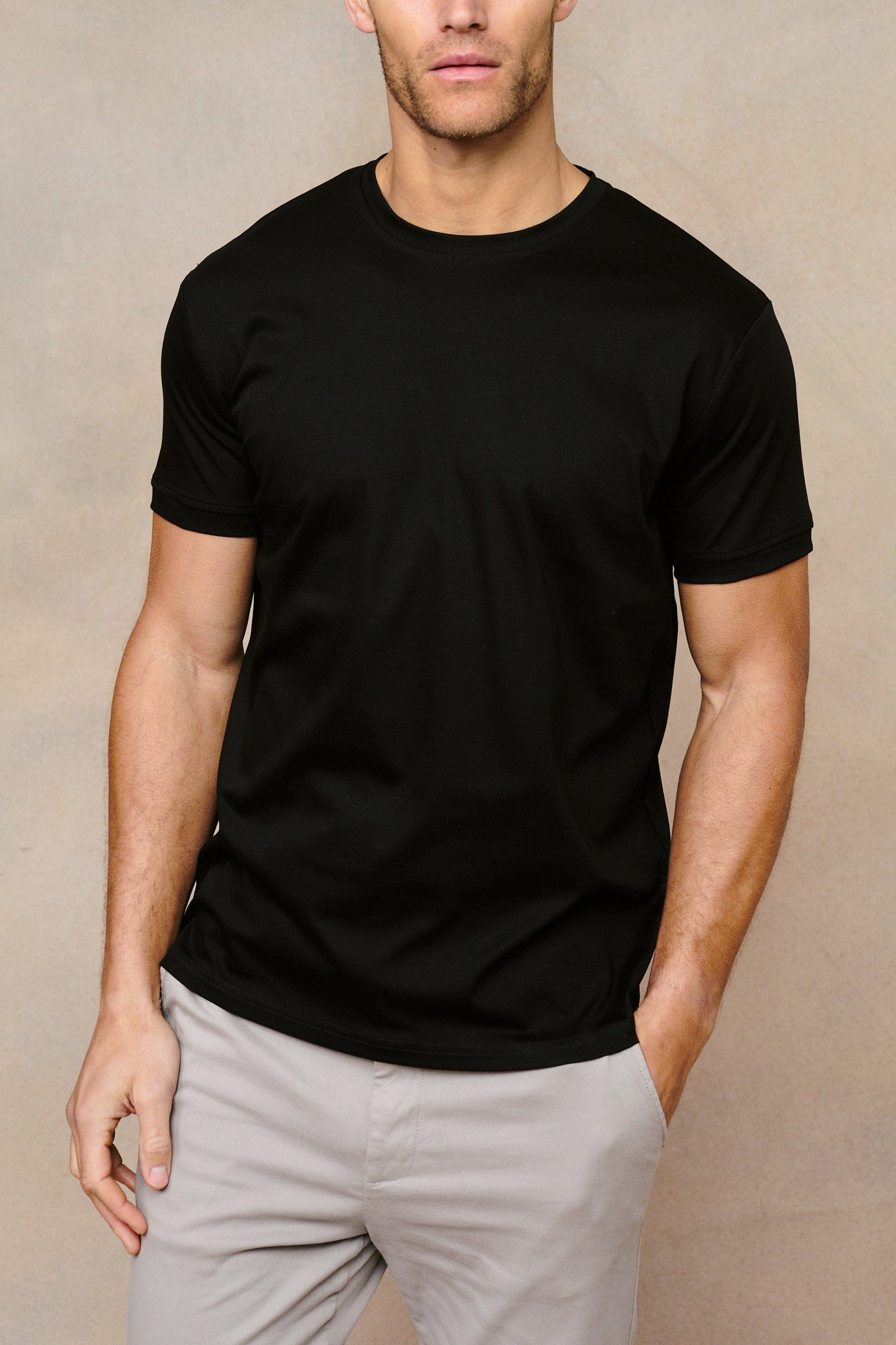 Man wearing a black mercerised cotton crew-neck t-shirt with light grey trousers.
