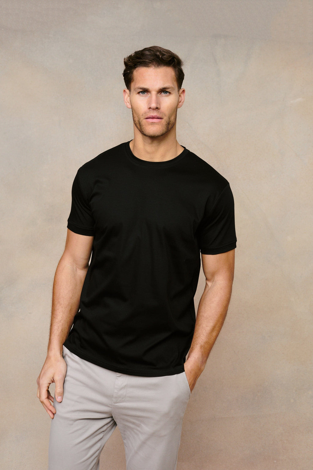 Man wearing a black Luxe Mercerised Cotton Crew-Neck T-Shirt with a subtle sheen, paired with light grey trousers.