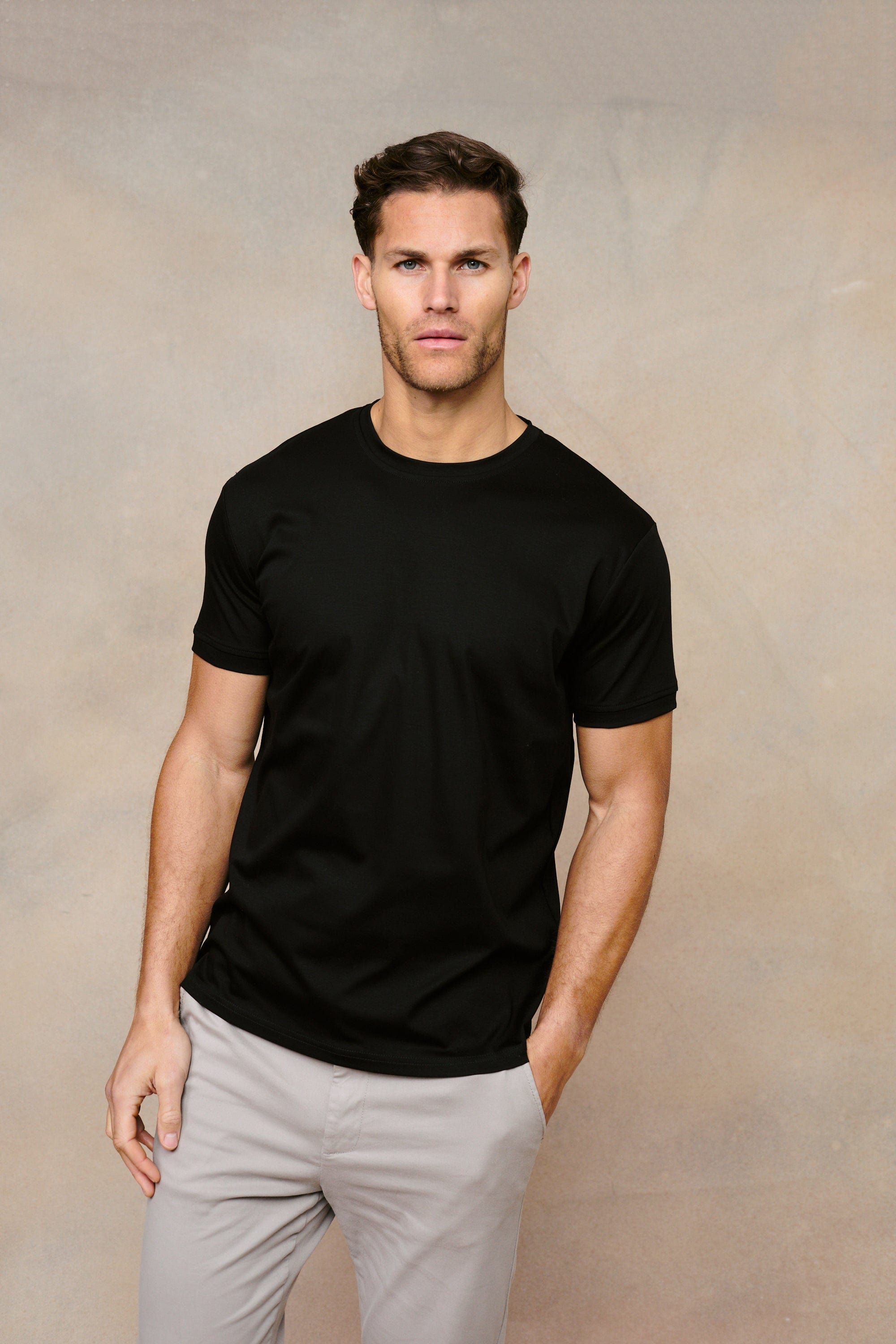 Man wearing a black Luxe Mercerised Cotton Crew-Neck T-Shirt with a subtle sheen, paired with light grey trousers.