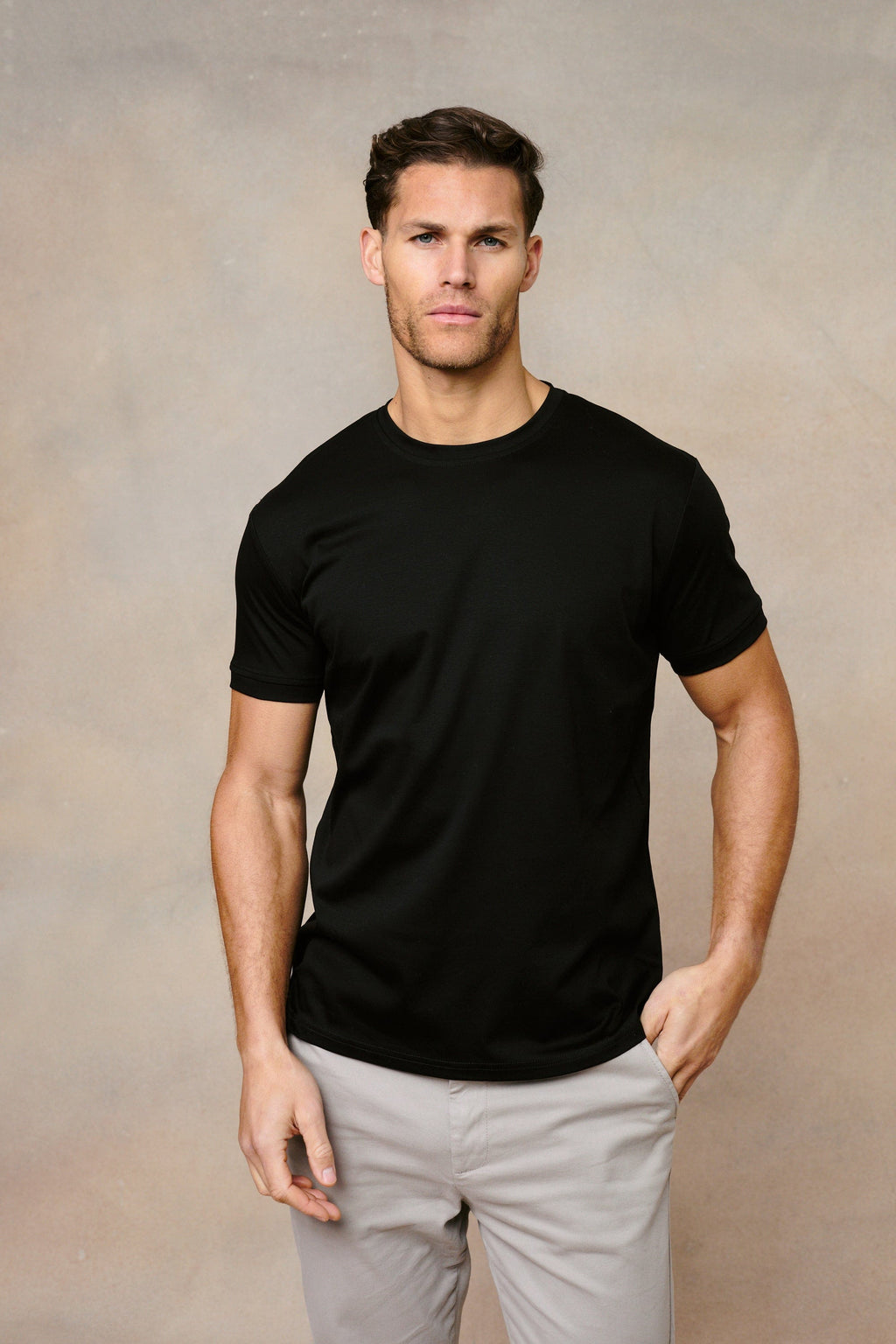 Man wearing a black Luxe Mercerised cotton crew-neck T-shirt with a subtle sheen and light grey chinos.