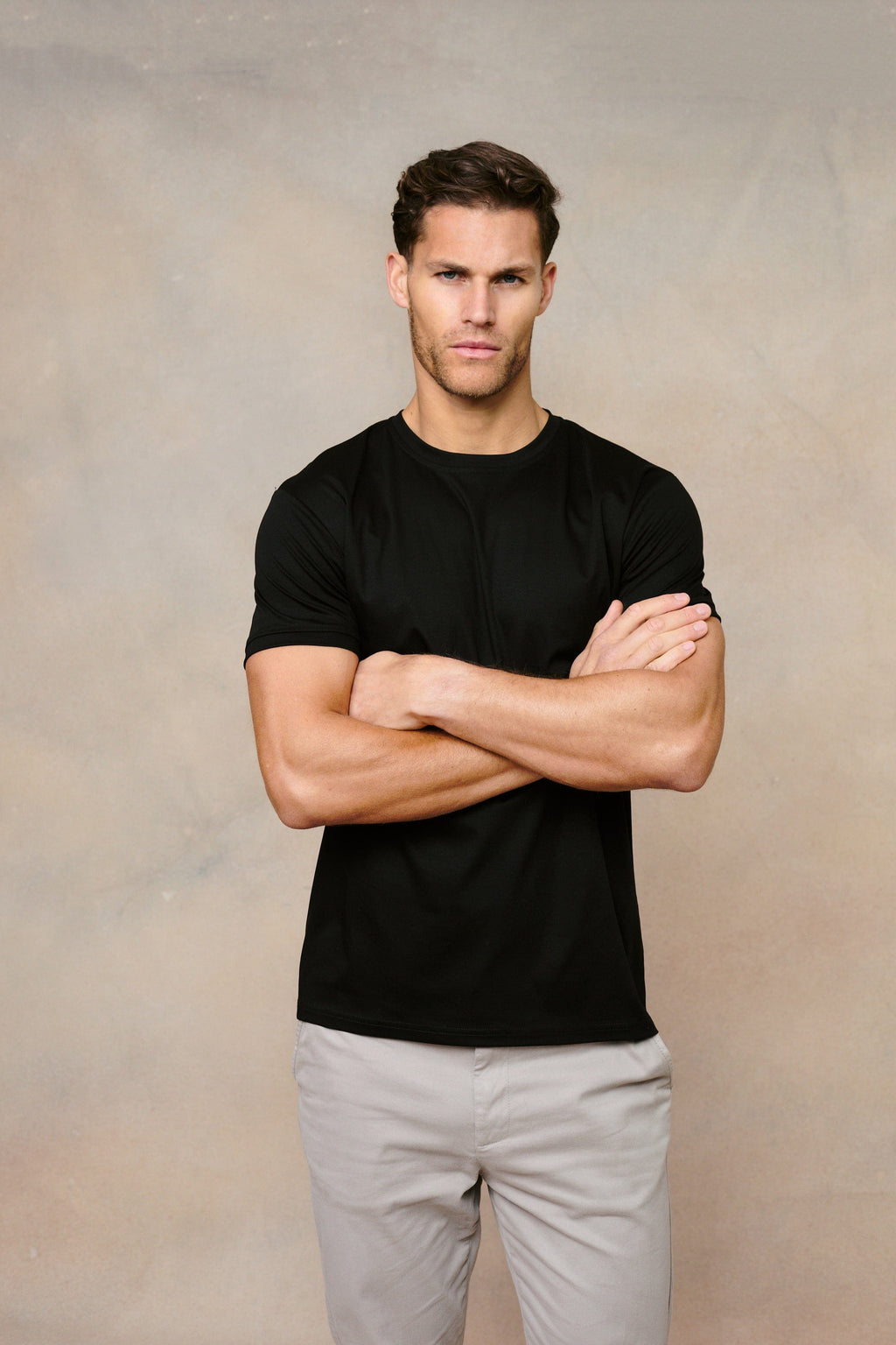 Man in a black Luxe Mercerised Cotton Crew-Neck T-Shirt with short sleeves, arms crossed.