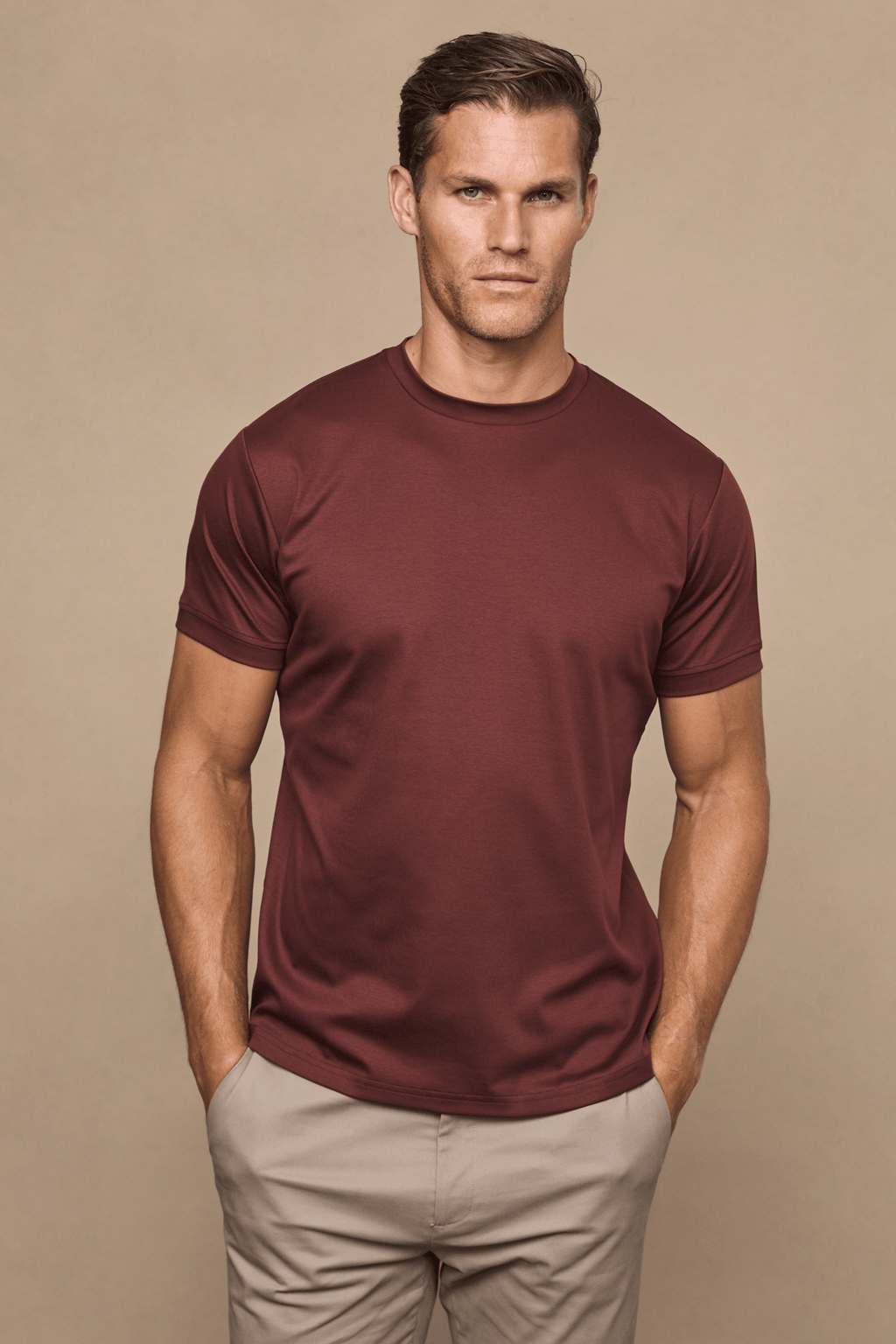 Man wearing a rust mercerised cotton crew-neck t-shirt with a subtle sheen and light beige trousers.