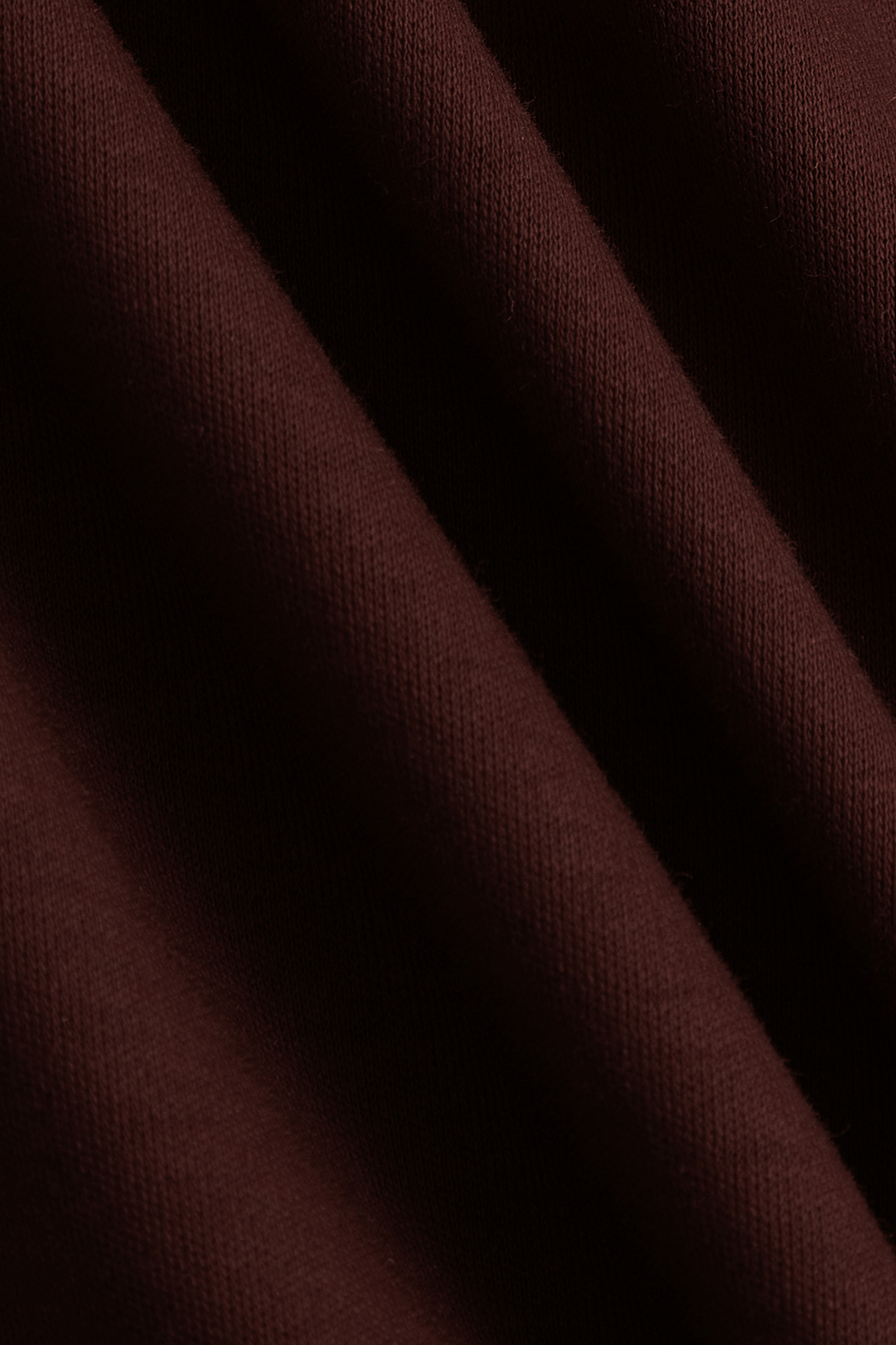 Close-up of rust mercerised cotton t-shirt fabric with subtle sheen and diagonal folds.