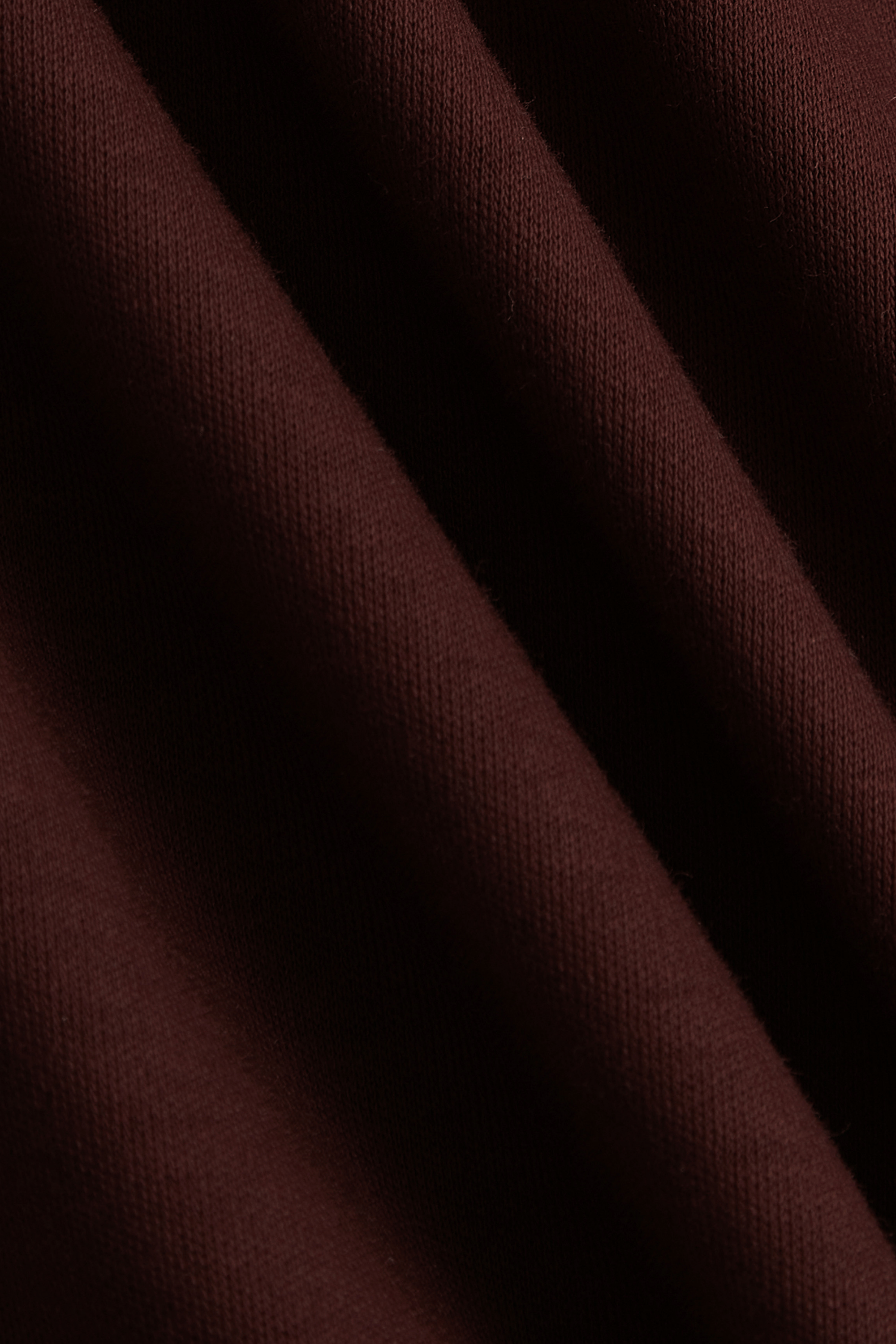 Close-up of rust mercerised cotton t-shirt fabric with subtle sheen and diagonal folds.