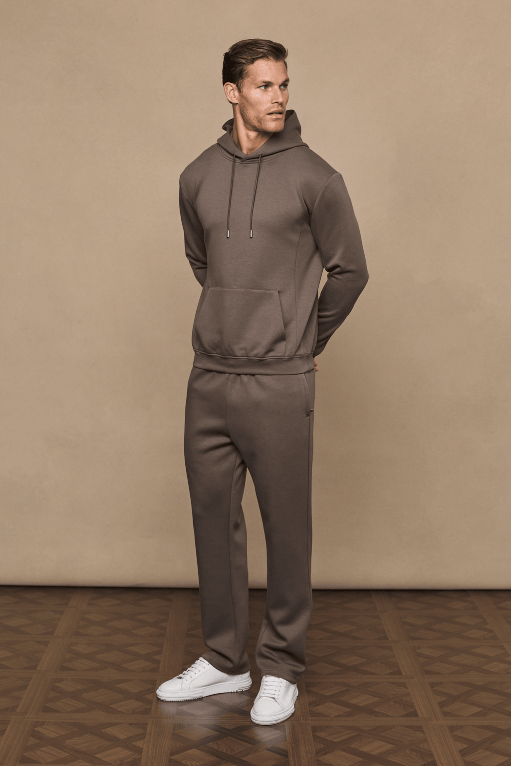 Man wearing a Luxe Straight Leg Jogger in Burnt Olive with a matching hoodie and white sneakers.