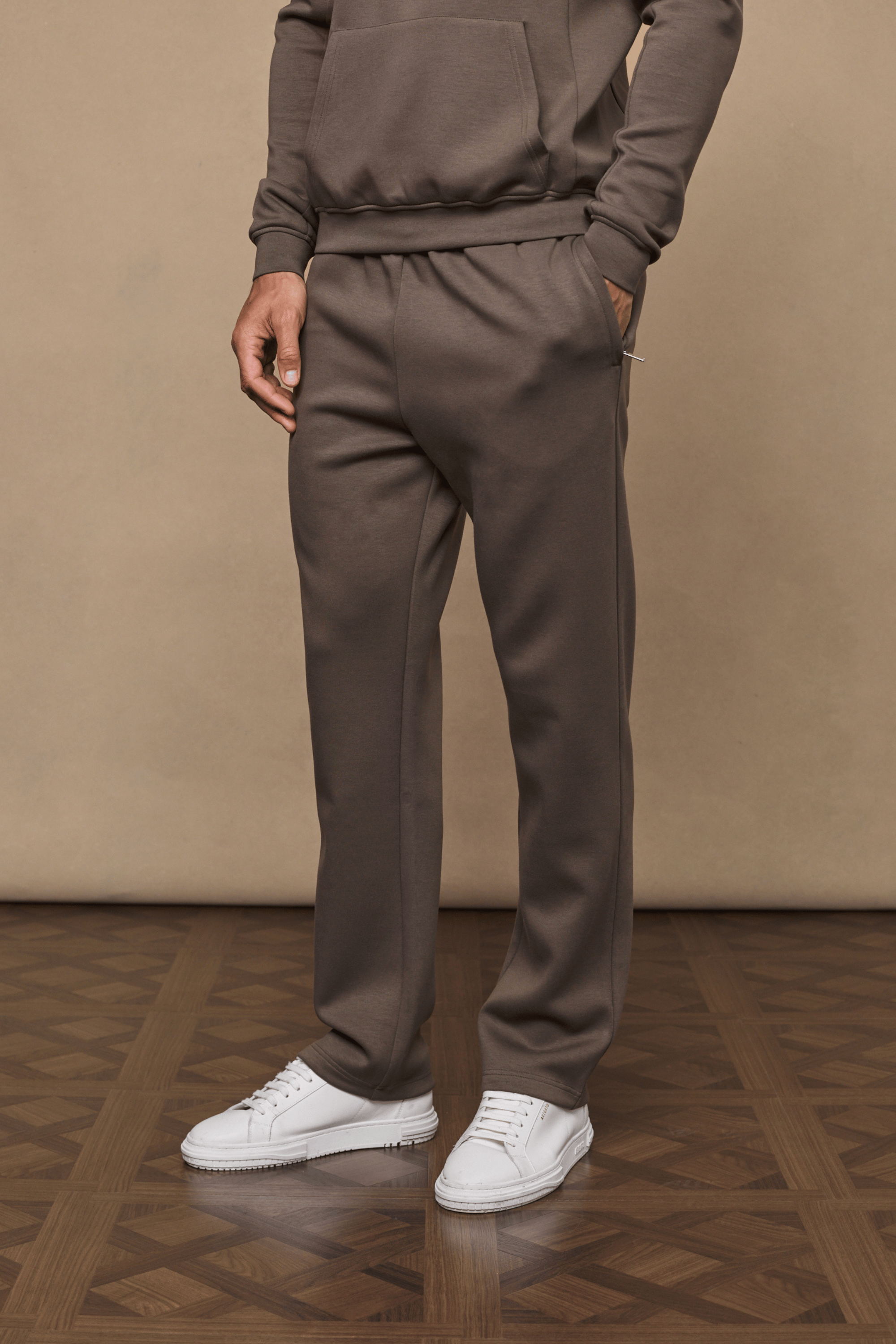 Man wearing Luxe Straight Leg Jogger in Burnt Olive, made from soft Luxe Fabric, with side pockets and white sneakers.
