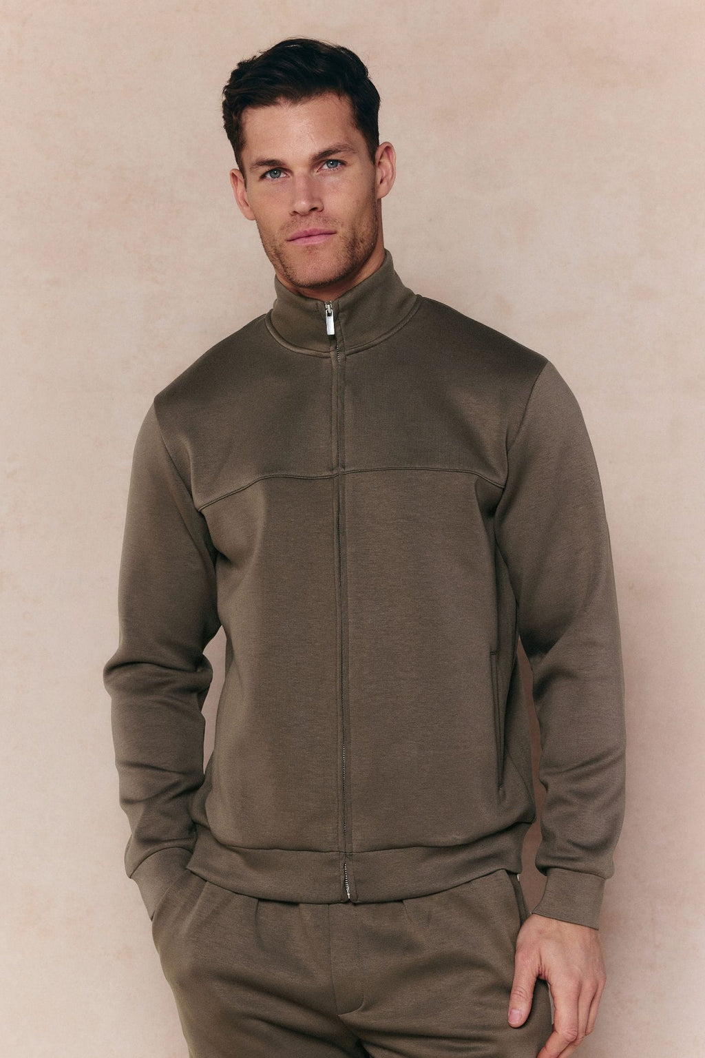 Man wearing a burnt olive Luxe Zip Through Jacket with metal hardware and matching pants.