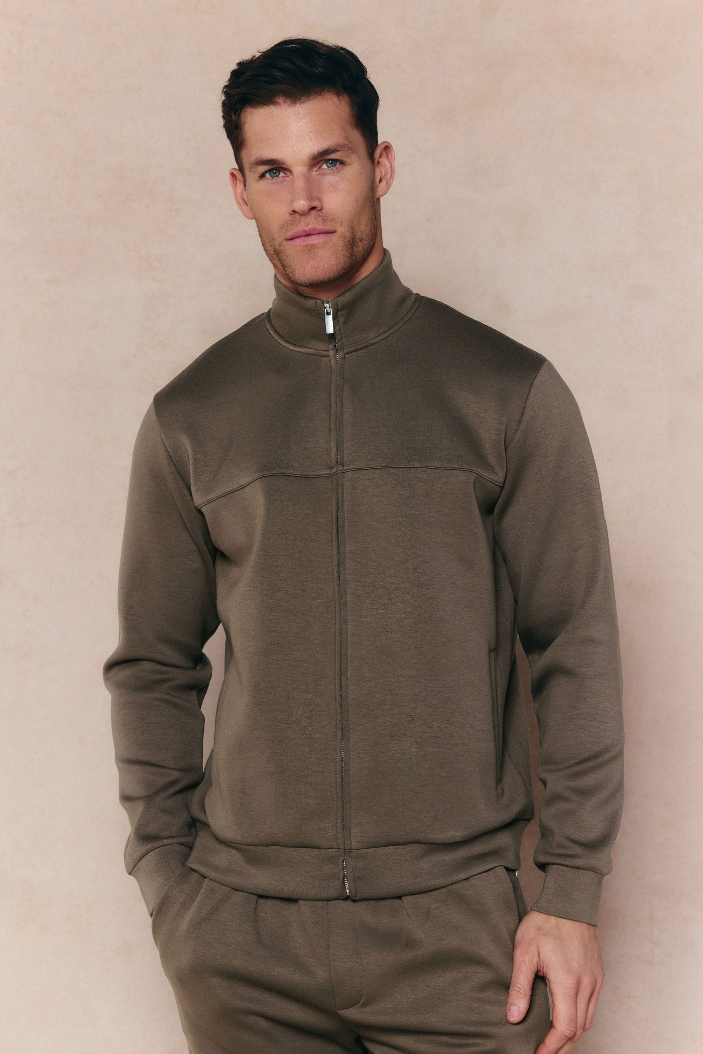 Man wearing a burnt olive Luxe Zip Through Jacket with metal hardware and matching pants.