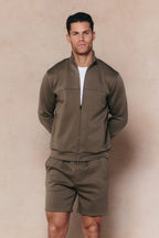 Man in a burnt olive Luxe Zip Through Jacket and matching shorts, showcasing the premium fabric and paneled design.