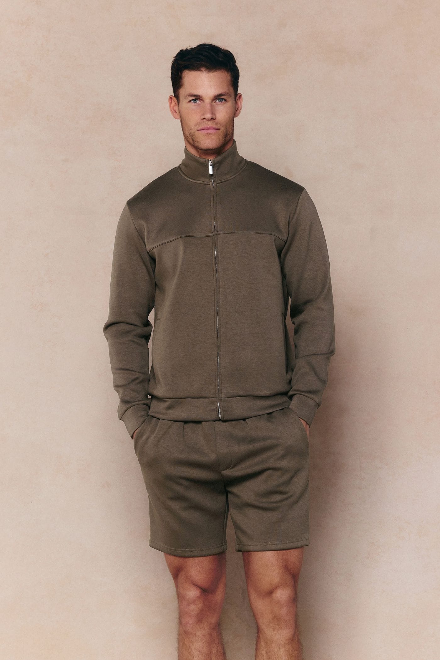 Man in Burnt Olive Luxe Zip Through Jacket and matching shorts, featuring metal hardware.